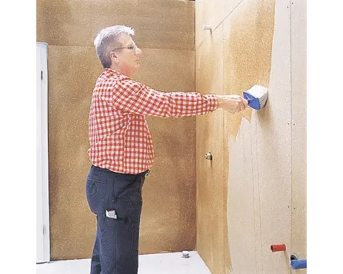 Mann trägt mit einer Bürste Beschichtung auf eine Wand auf