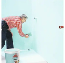 Ein Mann trägt Spachtelmasse auf eine Wand auf, im Vordergrund ein Eimer mit Spachtelmasse