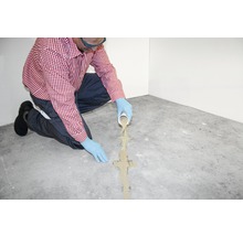 Eine Person trägt Handschuhe und schüttet Ausgleichsmasse auf einen Betonboden.