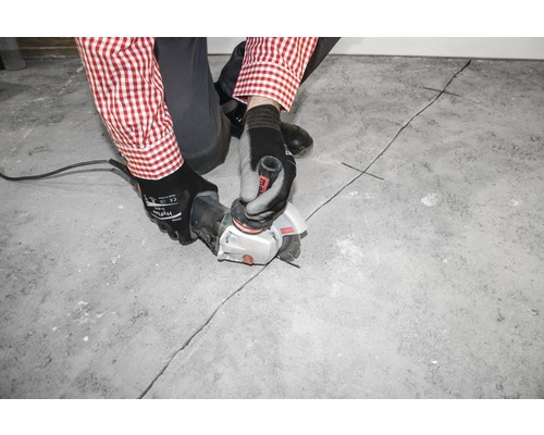 Eine Person schneidet mit einem Winkelschleifer eine Fuge in einen Betonboden.