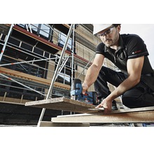 Ein Mann sägt mit einer Stichsäge ein Holzbrett auf einer Baustelle.