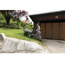 Frau schiebt eine Sackkarre mit Säcken durch den Garten.