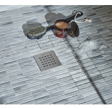 Detailaufnahme einer Dusche mit Bodenfliesen, Duschabfluss, Bürste, Badezusatz und Seifenschaum