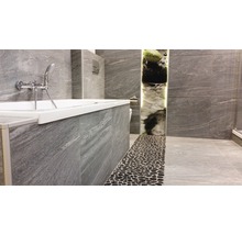 Badezimmer mit Badewanne, grauen Fliesen und Kieselboden