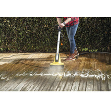 Eine Person reinigt eine Holzterrasse mit einem elektrischen Terrassenreiniger.
