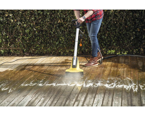 Eine Person reinigt eine Holzterrasse mit einem elektrischen Terrassenreiniger.