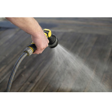 Person bewässert Holzboden mit Gartenschlauch und Spritzpistole