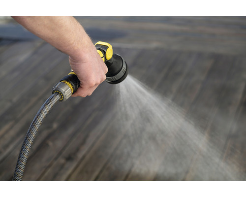 Person bewässert Holzboden mit Gartenschlauch und Spritzpistole