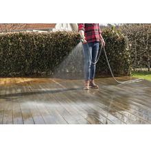 Eine Person reinigt eine Holzterrasse mit einem Wasserschlauch.