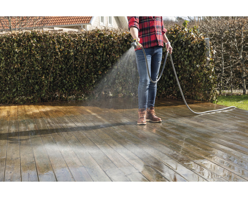 Eine Person reinigt eine Holzterrasse mit einem Wasserschlauch.