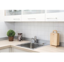 Küchenszene mit Spüle, Armatur, Schneidebrettern und Dekoration auf einer hellen Arbeitsplatte vor weißem Fliesenspiegel