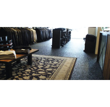 Innenansicht eines Bekleidungsgeschäfts mit Kleiderständern, Regalen und einem Teppich