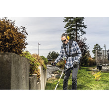 Mann mit Schutzbrille und Gehörschutz verwendet einen Rasentrimmer im Garten.