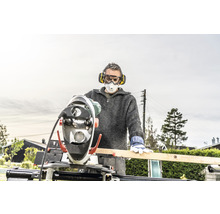 Mann mit Gehörschutz, Schutzbrille und Atemschutzmaske arbeitet mit einer Kappsäge an einem Holzbrett