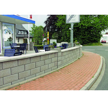 Eine graue Mauer aus Betonsteinen säumt den Weg vor einem Gebäude.