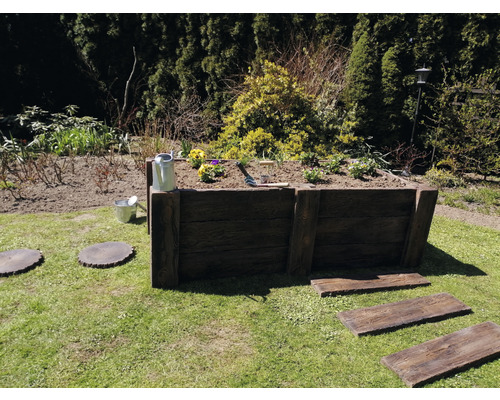 Hochbeet aus Holz im Garten mit Bepflanzung, Gießkanne und Gartenwerkzeug