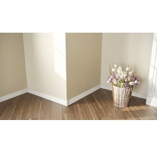 Ecke eines hellen Raumes mit Holzfußboden, weißen Fußleisten und einem Blumenstrauß in einem Topf