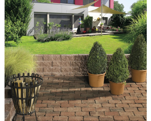 Gestalteter Garten mit Pflanzen, Pflastersteinen, Stützmauer und Feuerkorb