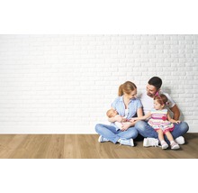 Eine Familie sitzt vor einer Wand aus Ziegelsteinen auf einem Holzboden.