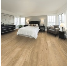 Schlafzimmer mit Holzboden, Bett, Kommode und Sessel.