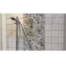 Detailaufnahme eines Duschkopfes vor einem Hintergrund aus Kieselsteinen und Fliesen