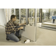 Mann befestigt Gipskartonplatte mit Schraubendreher an Metallständerwerk