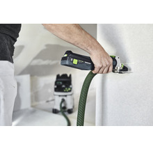 Eine Person benutzt ein Akku-Multitool an einer Wand. Ein Staubsauger ist im Hintergrund zu sehen.