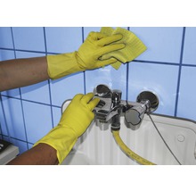 Reinigungskraft mit Gummihandschuhen reinigt Waschbecken und Fliesen mit einem Schwamm