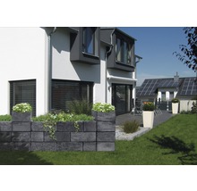 Graue Gartenmauer aus Betonsteinen mit Bepflanzung vor einem Wohnhaus.