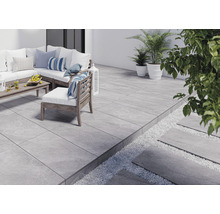 Terrasse mit grauen Fliesen, Gartenmöbeln und Pflanzen.