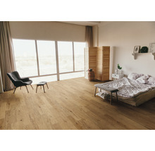 Heller Schlafzimmerraum mit Holzboden, Sessel, Bett und großem Fenster.