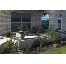 Terrasse mit Gartenmöbeln und bepflanzten Blumenkübeln vor einem Haus mit Backsteinfassade.