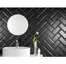 Badezimmer mit Waschbecken, rundem Spiegel und Wandfliesen im Fischgrätenmuster