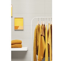 Dekorativer Raum mit geriffelten Wandpaneelen, Kleiderständer mit gelber Kleidung, Regal mit gelben Textilien und gerahmten Bildern