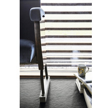 Detailaufnahme eines Sessels neben einem Fenster mit Jalousie, im Vordergrund Bücher und eine Tasse.