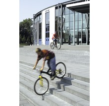 Zwei Personen fahren mit Fahrrädern vor einem Gebäude Treppen hinunter.