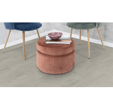 Szene mit einem runden, gesteppten Hocker mit Stauraum, auf dem eine Schale und Bücher liegen, sowie zwei Stühlen mit Holzbeinen.