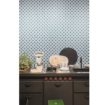 Küchenszene mit Spüle, Kochfeld, Waage und Geschirr vor einer gemusterten Wand