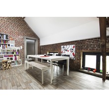 Helles Esszimmer mit Esstisch, Bank, Stühlen und Bücherregal vor Ziegelwand