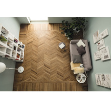 Ansicht von oben eines Zimmers mit einem Fischgrätenmuster-Holzboden, einem Bücherregal, einem Sofa, einem Beistelltisch und Wandkunst