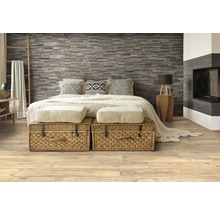 Schlafzimmer mit Steinwand, Holzboden und geflochtenen Truhen vor dem Bett