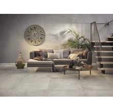 Wohnzimmer mit Sofa, Couchtisch, Uhr und Treppe in einem Interieur mit Fliesenboden.