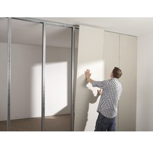 Ein Mann montiert eine Gipskartonplatte an einem Metallständerwerk im Innenbereich.