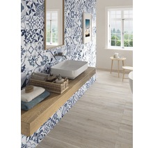 Helles Badezimmer mit Waschbecken, Spiegel, Fenster und blau-weiß gemusterten Fliesen