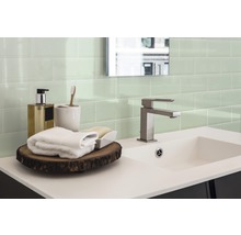 Badezimmer mit Waschbecken, Armatur, Handtüchern und grünen Fliesen