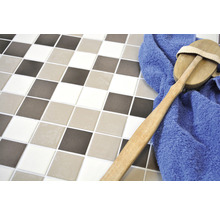 Quadratische Fliesen in verschiedenen Farbtönen mit einer Bürste und einem blauen Handtuch