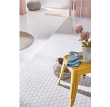 Badezimmer mit weißen, sechseckigen Bodenfliesen, gelbem Hocker, Handtuch und Badezimmeraccessoires.