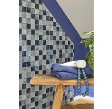 Badezimmerwand mit Mosaikfliesen in verschiedenen Blautönen, Handtuch und Dekoration auf einem Holzhocker.