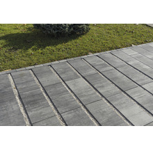 Außenbereich mit Pflastersteinen und Kiesstreifen neben einer Rasenfläche