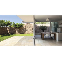 Helle Terrasse mit Natursteinmauer und Übergang zu einem Essbereich im Innenraum